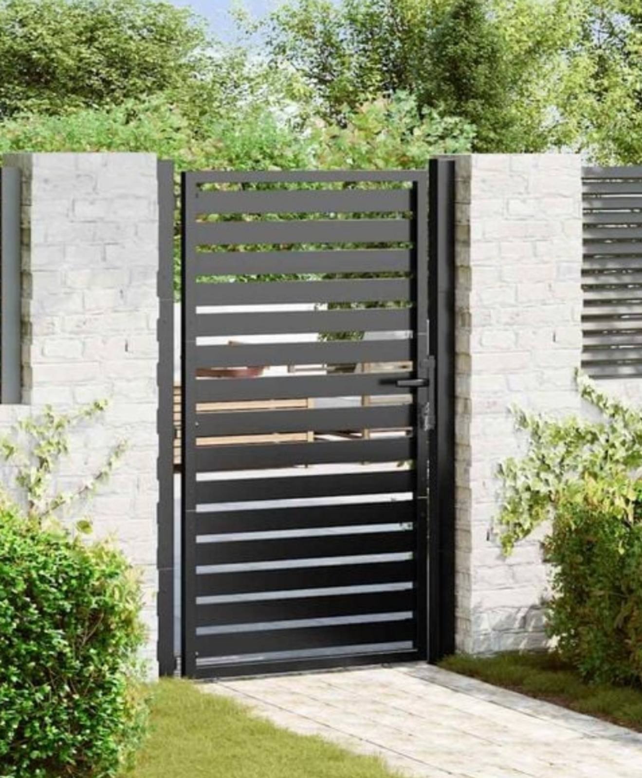 Nowoczesna, pozioma brama wjazdowa z czarnych profili, osadzona w białym, ceglanym murze. Minimalistyczny design, zieleń w tle.