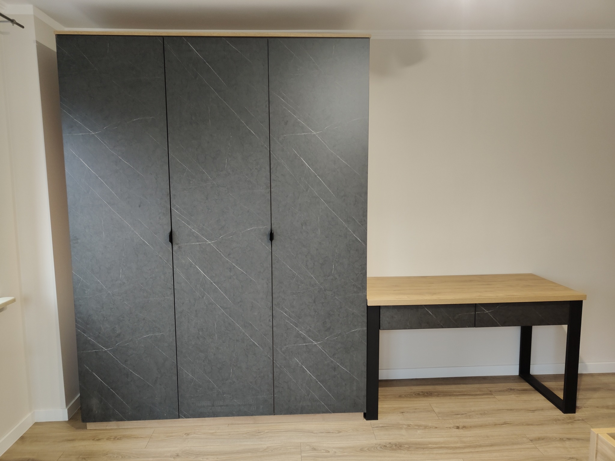 Nowoczesna szafa z szarymi drzwiami imitującymi marmur i biurko z drewnianym blatem na czarnych nogach, Radomsko. Minimalistyczny design, jasne wnętrze.