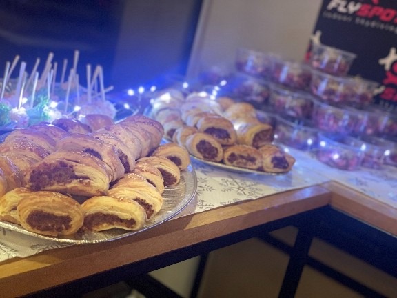 Słone przekąski z ciasta francuskiego na srebrnej tacy, obok mini-sałatki w przezroczystych pojemnikach, całość oświetlona niebieskimi lampkami.