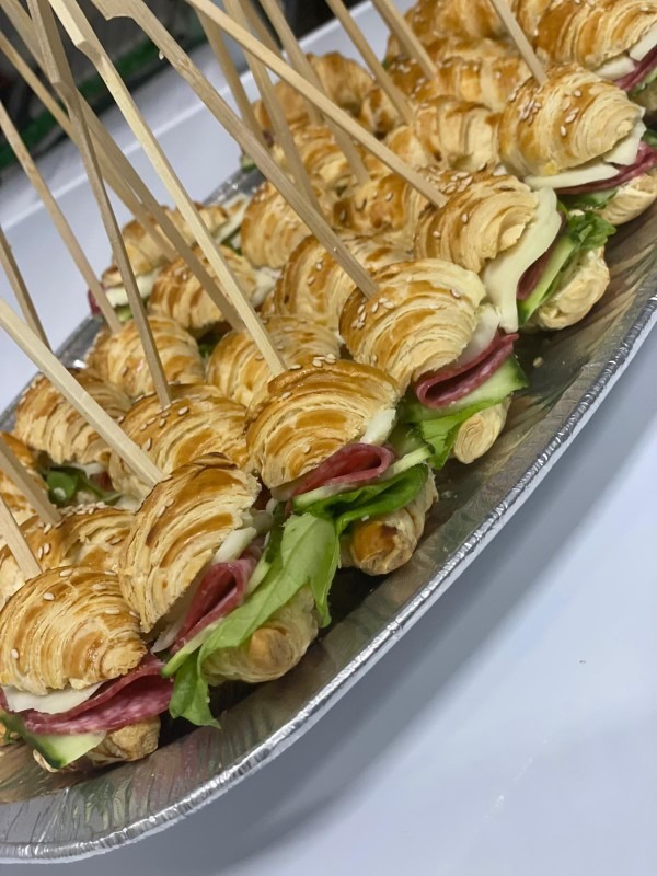 Kruche mini croissanty z salami, serem i warzywami, spięte wykałaczkami, ułożone na srebrnej tacy. Idealne jako przekąska na przyjęciu.