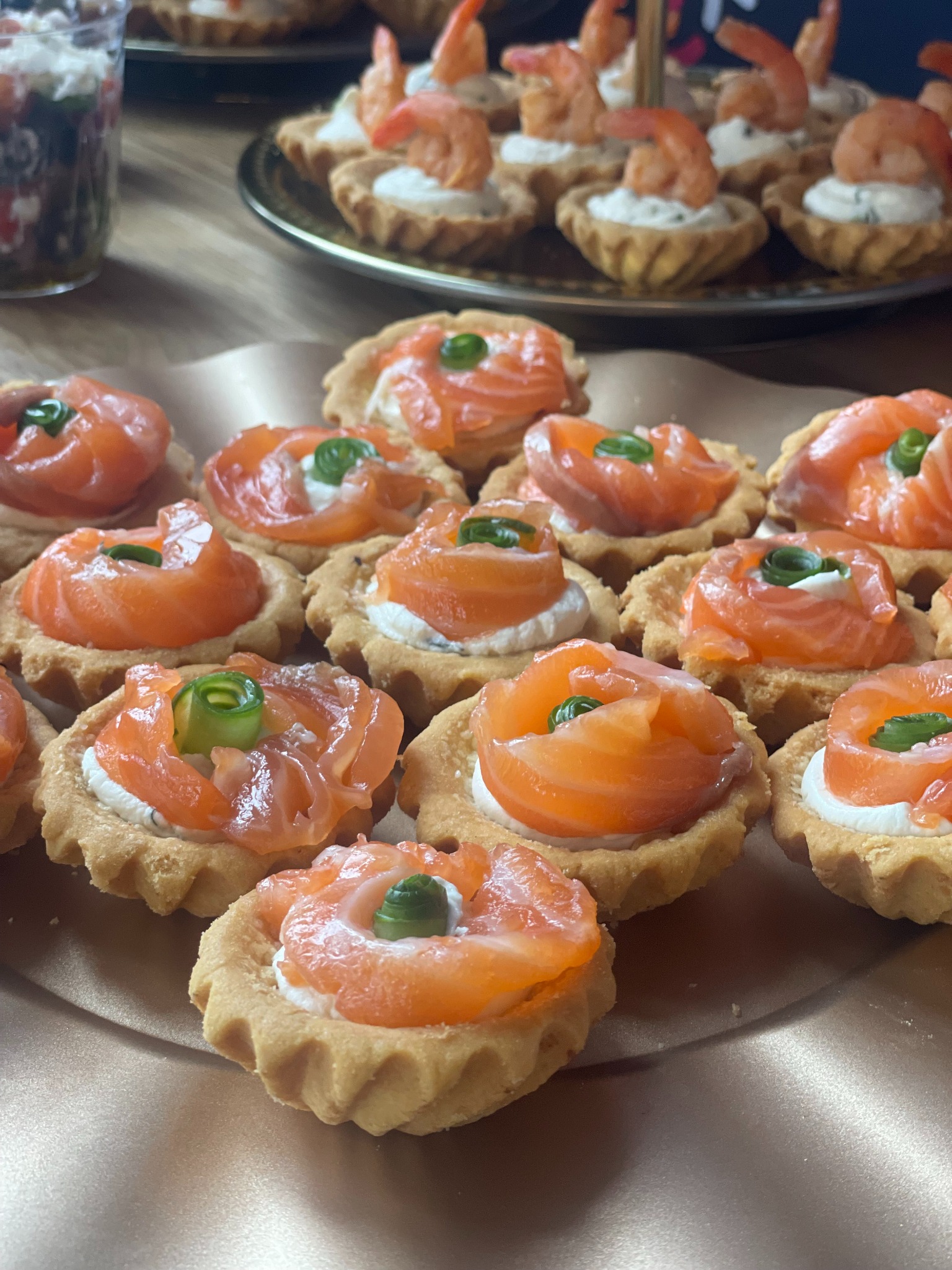 Tarty z łososiem i krewetkami na złotej tacy, zbliżenie. Eleganckie przekąski cateringowe z kremowym serem i zielonym akcentem, idealne na przyjęcie.