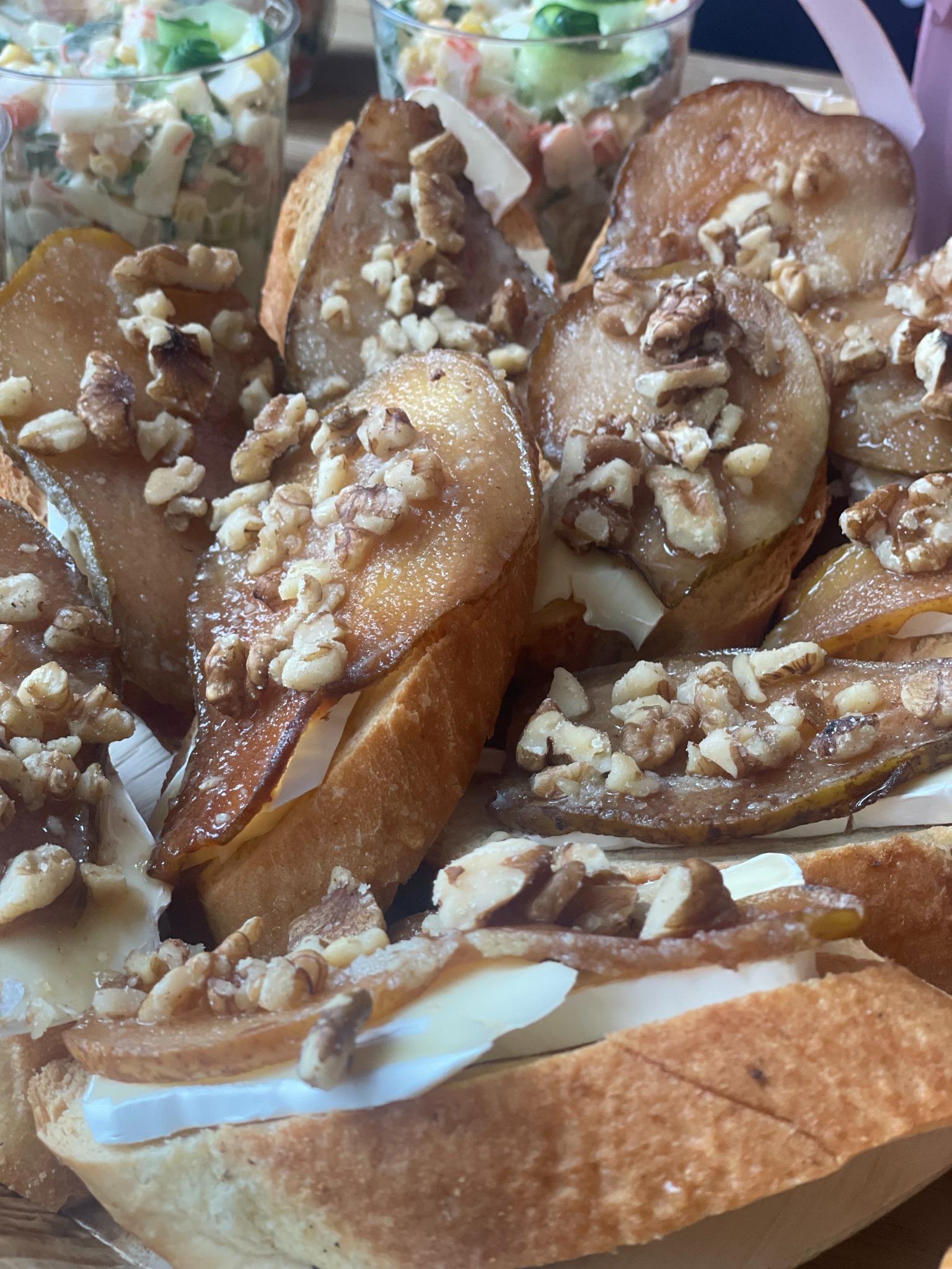 Baguette z karmelizowaną gruszką, serem brie i orzechami włoskimi. Eleganckie przekąski cateringowe na przyjęcie, widoczne też sałatki w tle.