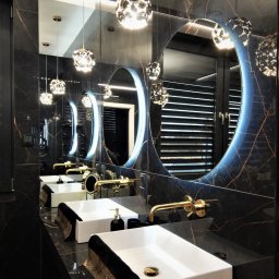 ArchiDESIGN STUDIO PROJEKTOWE arch. Maciej Tubielewicz - Elegancka łazienka z czarnym marmurem, złotą armaturą i okrągłymi lustrami z podświetleniem LED. Dwie białe umywalki i designerskie lampy wiszące.