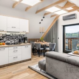 ArchiDESIGN STUDIO PROJEKTOWE arch. Maciej Tubielewicz - Jasna kuchnia z salonem na poddaszu: białe szafki, drewniane belki stropowe, okno z widokiem na las. Nowoczesny design z unikalnym backsplashiem z motywem zdjęć.