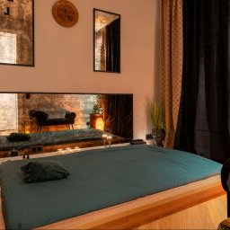 Blissful Massage Mokótow - Stylowe wnętrze gabinetu z łóżkiem do zabiegów, lustrami i dekoracjami. Zegar na ścianie, nastrojowe oświetlenie i zasłony tworzą relaksującą atmosferę.