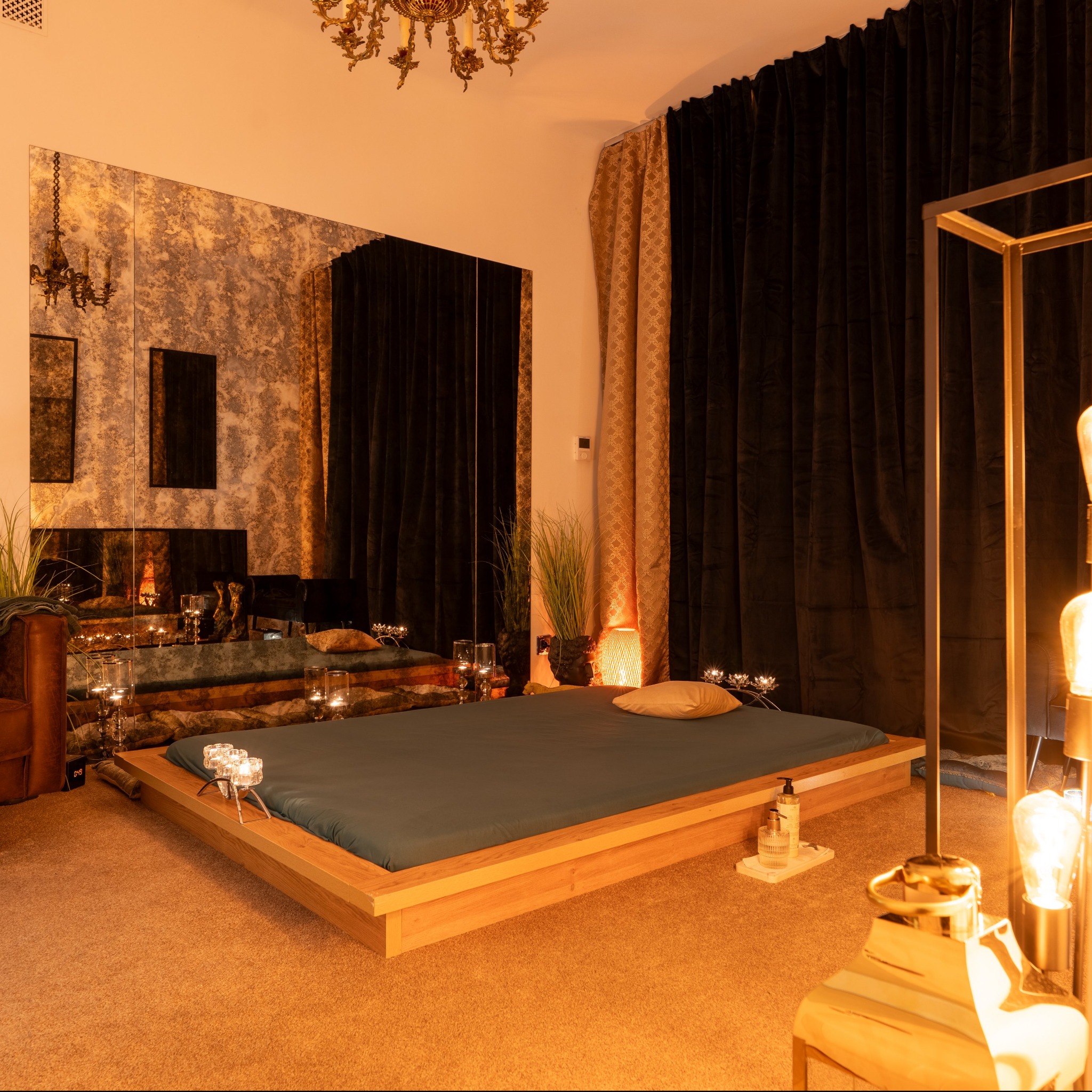 Luksusowe wnętrze gabinetu z łóżkiem do zabiegów, lustrzaną ścianą i świecami. Klimatyczne oświetlenie tworzy relaksującą atmosferę. Widoczne akcesoria do zabiegów.
