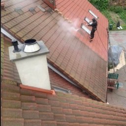 Usługi Dachowe - Czyszczenie dachu z dachówki ceramicznej myjką ciśnieniową. Widoczna różnica w kolorze między umytą a zabrudzoną częścią dachu. Praca na wysokości, zabezpieczenia.