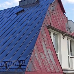 Usługi Dachowe - Częściowy widok dachu: połowa pomalowana na granatowo, druga w odcieniach czerwieni z widocznymi śladami użytkowania. Widoczne okna i antena satelitarna.