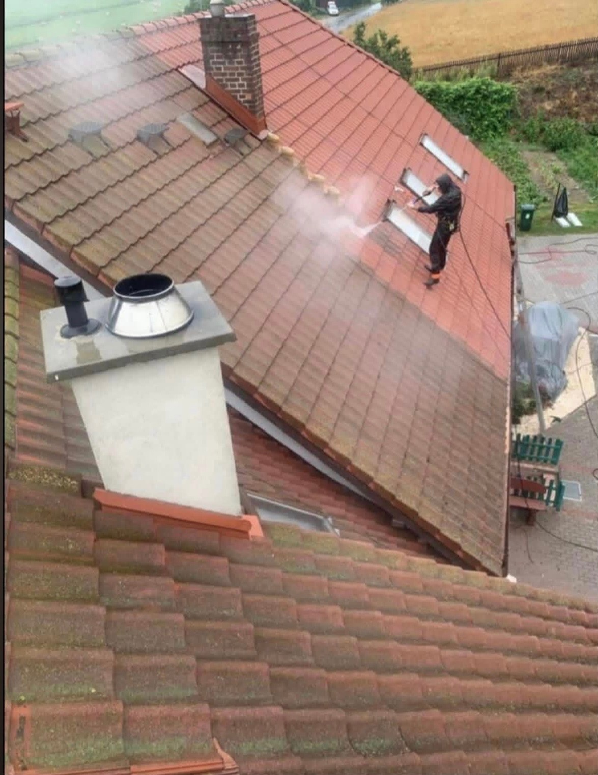 Czyszczenie dachu z dachówki ceramicznej myjką ciśnieniową. Widoczna różnica w kolorze między umytą a zabrudzoną częścią dachu. Praca na wysokości, zabezpieczenia.
