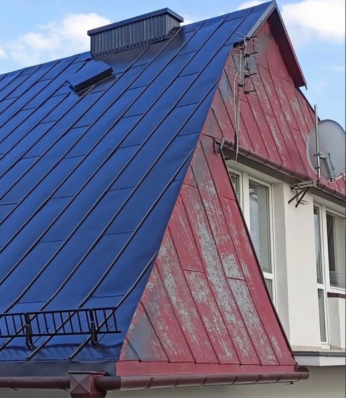 Częściowy widok dachu: połowa pomalowana na granatowo, druga w odcieniach czerwieni z widocznymi śladami użytkowania. Widoczne okna i antena satelitarna.