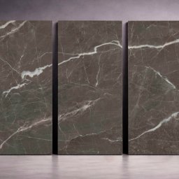 Lamaro - Trzy duże, pionowe płyty z ciemnego marmuru z białymi żyłami, ustawione obok siebie na szarym tle. Obok nich sylwetka człowieka w formie szkicu.