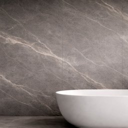 Lamaro - Nowoczesna łazienka z wolnostojącą białą wanną na tle ściany wyłożonej szarymi płytkami imitującymi marmur z delikatnym, jasnym żyłkowaniem i chromowaną armaturą.