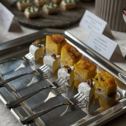 LUO SPÓŁKA Z OGRANICZONĄ ODPOWIEDZIALNOŚCIĄ - Srebrna taca z serami brie z orzechami i kawałkami ciasta na widelcach, elegancko podane, w tle inne przekąski i etykiety z nazwami.