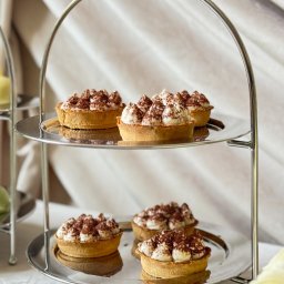 LUO SPÓŁKA Z OGRANICZONĄ ODPOWIEDZIALNOŚCIĄ - Dwupoziomowy srebrny etażer z mini tartaletkami tiramisu na białym obrusie i kremowym tle. Elegancki deser na przyjęcie.