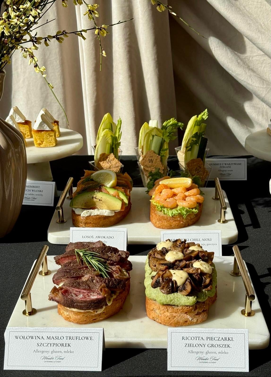 Elegancki catering: kanapki z łososiem i awokado, wołowiną truflową, ricottą i pieczarkami, hummusem warzywnym. Marmurowe tace, złote uchwyty, subtelne dekoracje.