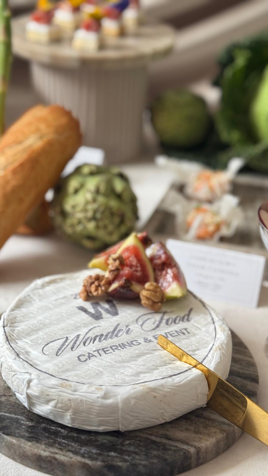 Dekoracyjny stół z serem brie z figami i orzechami na marmurowej desce, bagietką, karczochami i przekąskami w tle. Elegancki catering na imprezę.