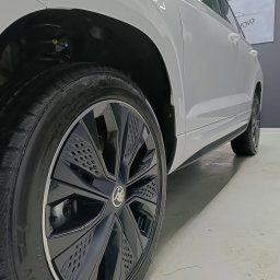 Izdebski Studio - Auto Detailing Warszawa - Błyszczące, czarne felgi aluminiowe z logo Skody na białym samochodzie. Widoczne detale opony i nadkola. Auto po detailingu, w studio z oświetleniem LED.