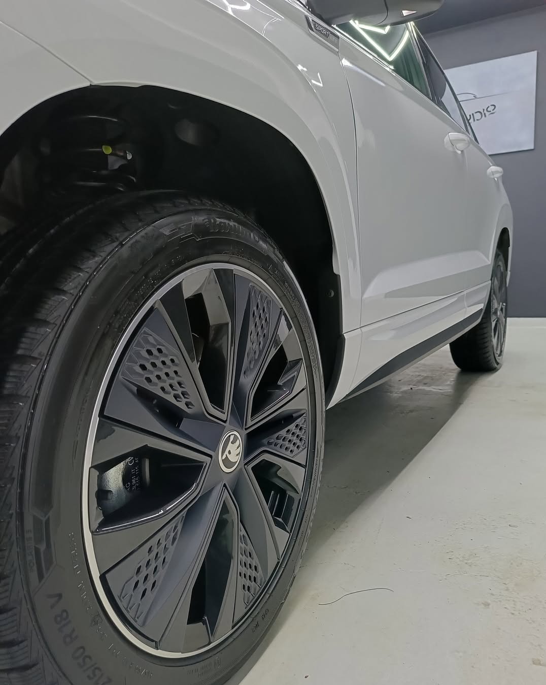 Błyszczące, czarne felgi aluminiowe z logo Skody na białym samochodzie. Widoczne detale opony i nadkola. Auto po detailingu, w studio z oświetleniem LED.