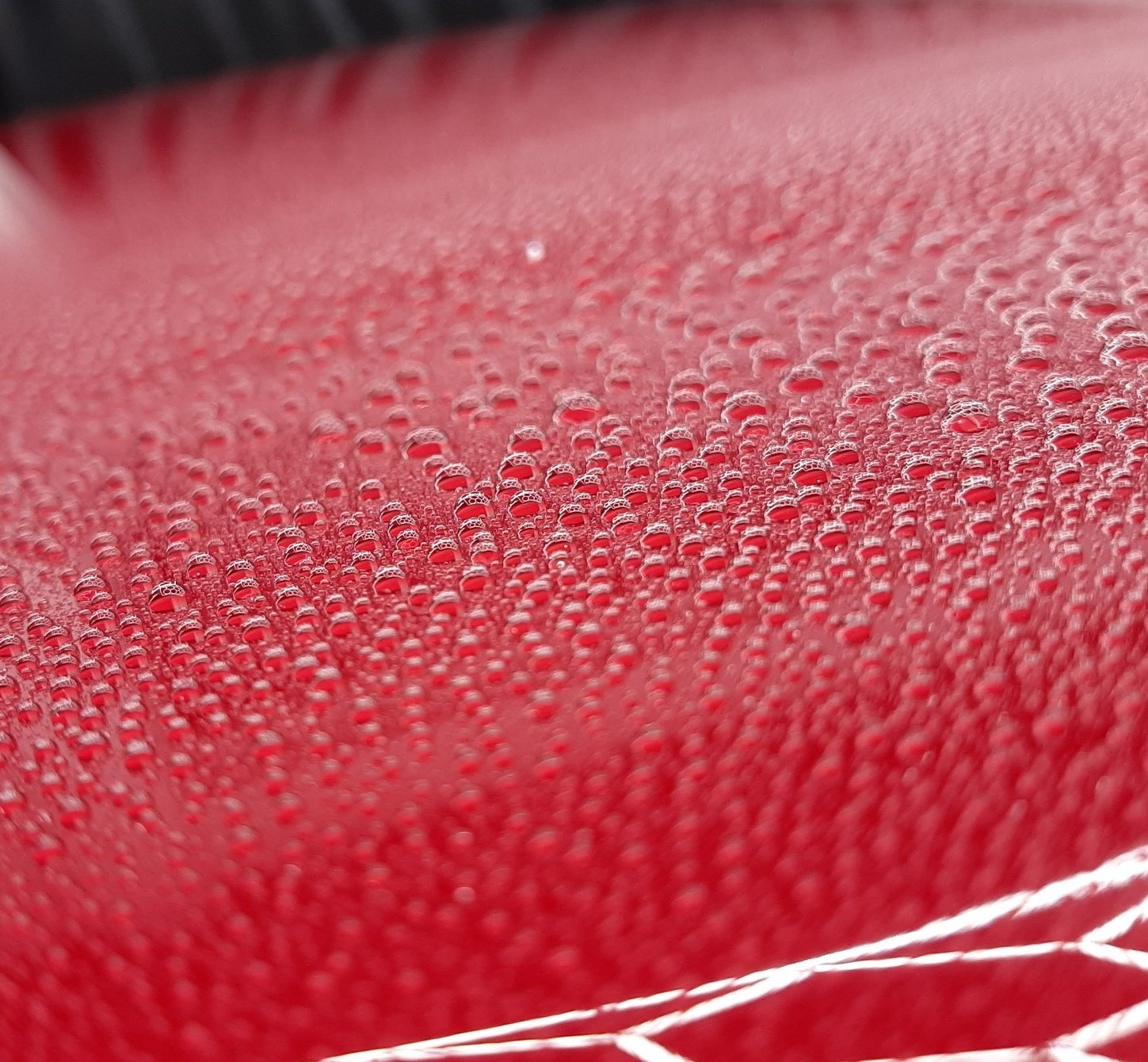 Czerwony lakier auta po nałożeniu powłoki hydrofobowej w Warszawie. Widoczne krople wody na powierzchni, świadczące o właściwościach ochronnych.