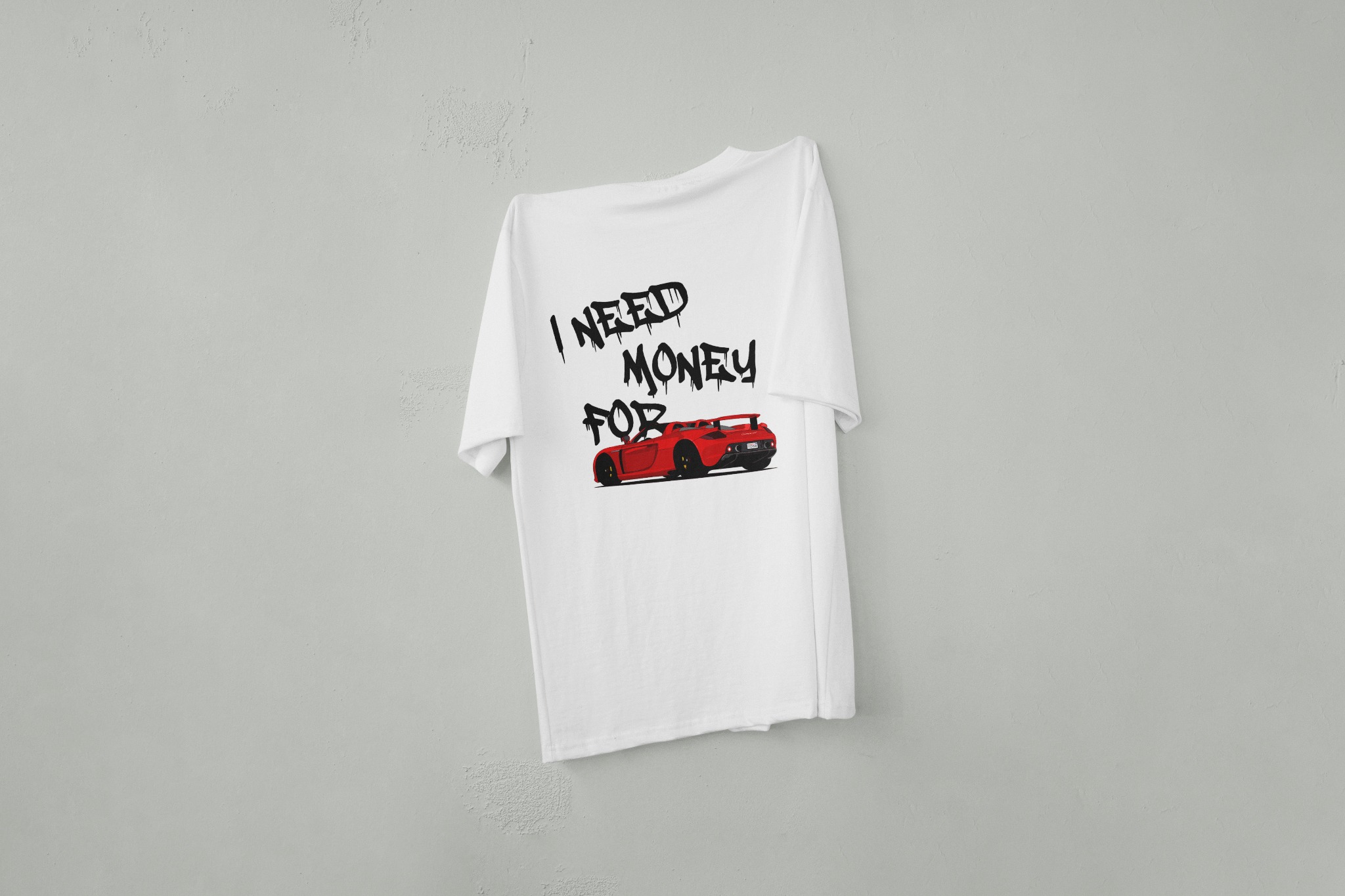 Biała koszulka z nadrukiem czerwonego sportowego auta i napisem 'I need money for...' w stylu graffiti, wisząca na szarej ścianie. Prezentacja nadruku na odzieży.