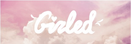 Biały, ręcznie pisany napis 'Girled' z sercem na tle pastelowego, różowo-białego nieba z chmurami. Delikatna, kobieca estetyka.