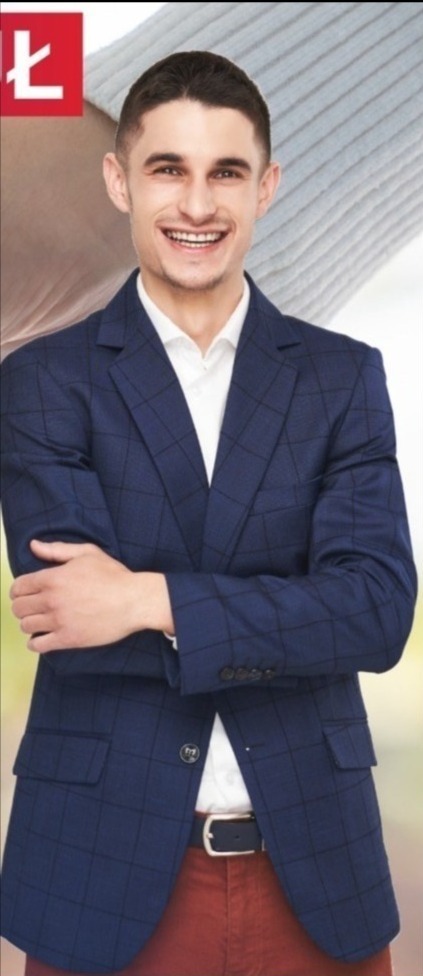 Uśmiechnięty agent nieruchomości w granatowej marynarce w kratę, białej koszuli i bordowych spodniach, z założonymi rękami, na rozmytym tle.