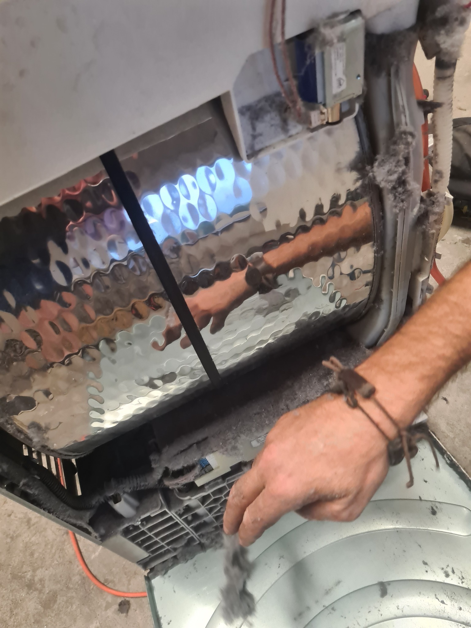 Wnętrze pralki automatycznej z nagromadzonymi kłaczkami, widoczna dłoń usuwająca zanieczyszczenia. Perspektywa z góry, oświetlenie naturalne.