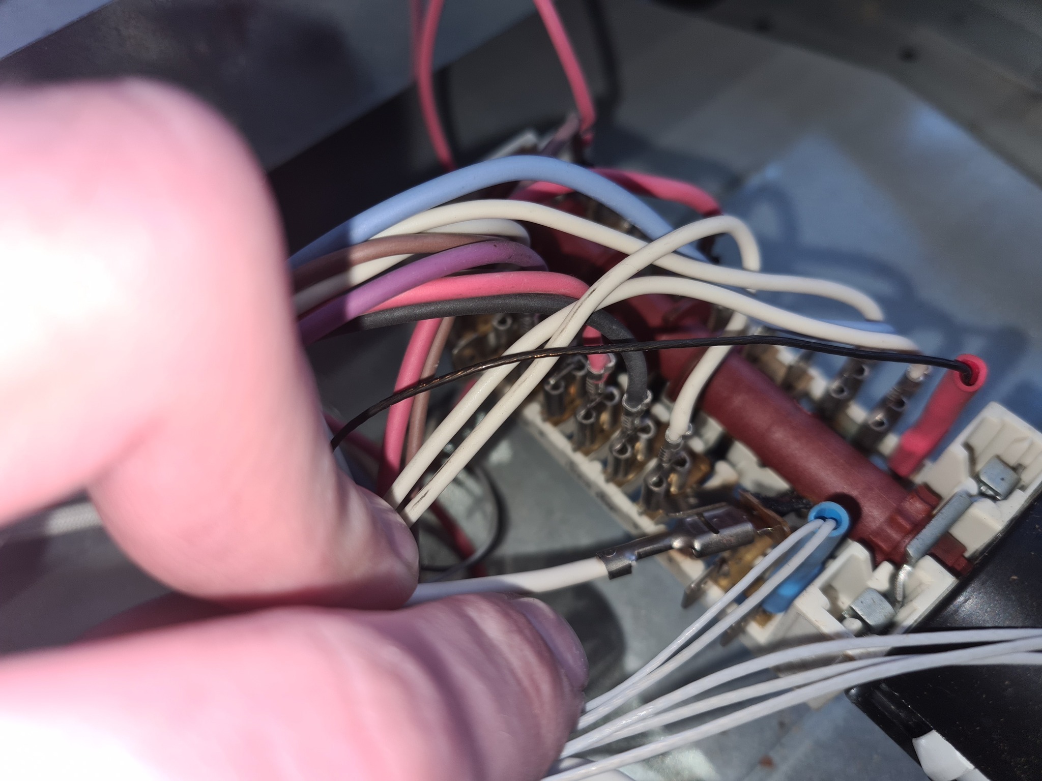 Zbliżenie na rękę serwisanta pracującego nad podłączeniem przewodów wewnątrz urządzenia AGD. Widoczne kolorowe kable i złącza.