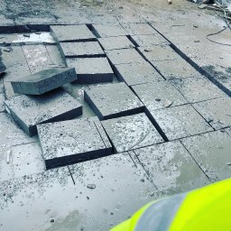 Pol - Cut Technika Diamentowa Jacek Suchodolski - Fragment podłogi z wyciętymi kwadratami, mokra powierzchnia, widoczne ślady cięcia, w tle paleta z materiałami budowlanymi, ujęcie z góry.