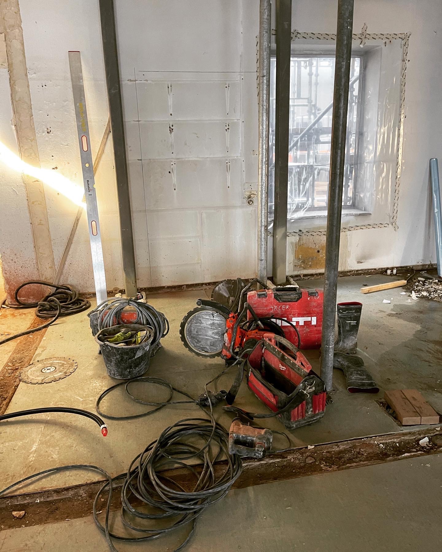 Przygotowane stanowisko pracy z narzędziami Hilti i poziomnicą, zabezpieczone okno folią, ślady po demontażu ścian działowych, widoczne zbrojenia.