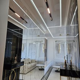 Geblon - Eleganckie wnętrze salonu z lustrzanymi ścianami, oświetleniem LED i dekoracyjnymi lampami wiszącymi. Widoczny fragment sofy i stolików kawowych w jasnej kolorystyce.