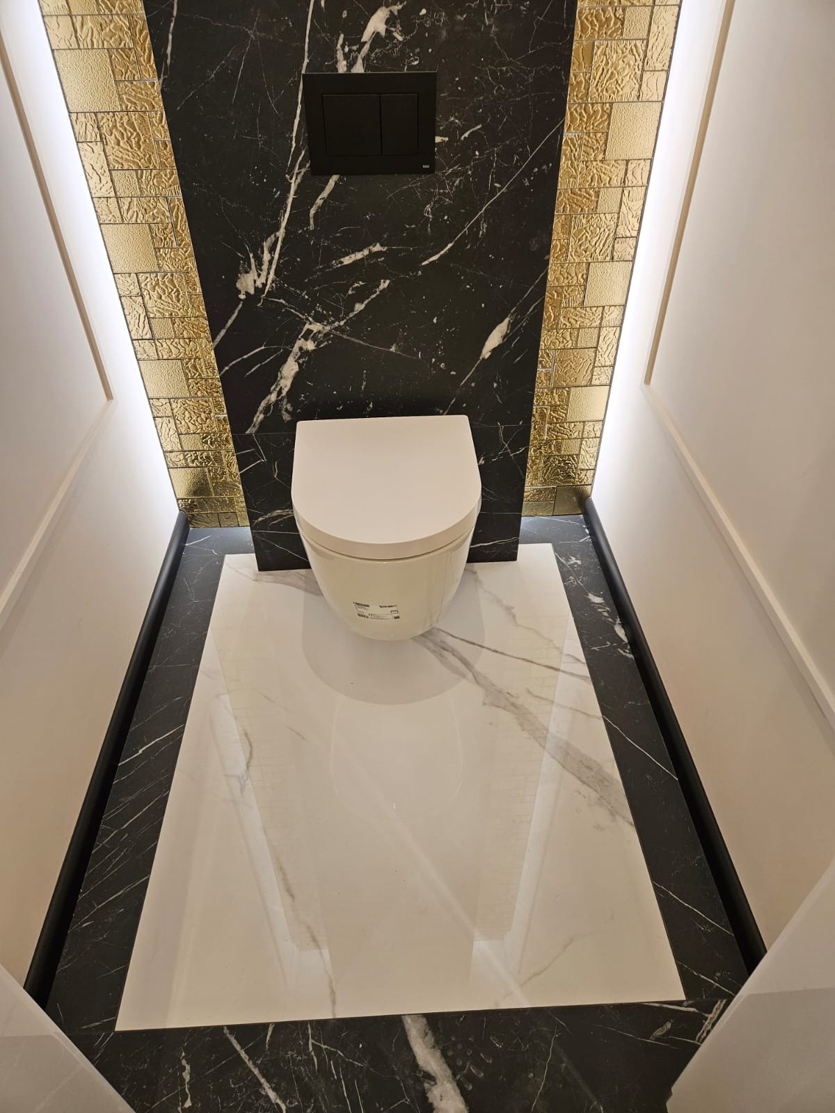 Nowoczesna toaleta w Bydgoszczy: biała miska WC na tle marmurowej podłogi i ściany z czarnego marmuru, akcentowana złotymi, dekoracyjnymi płytkami.