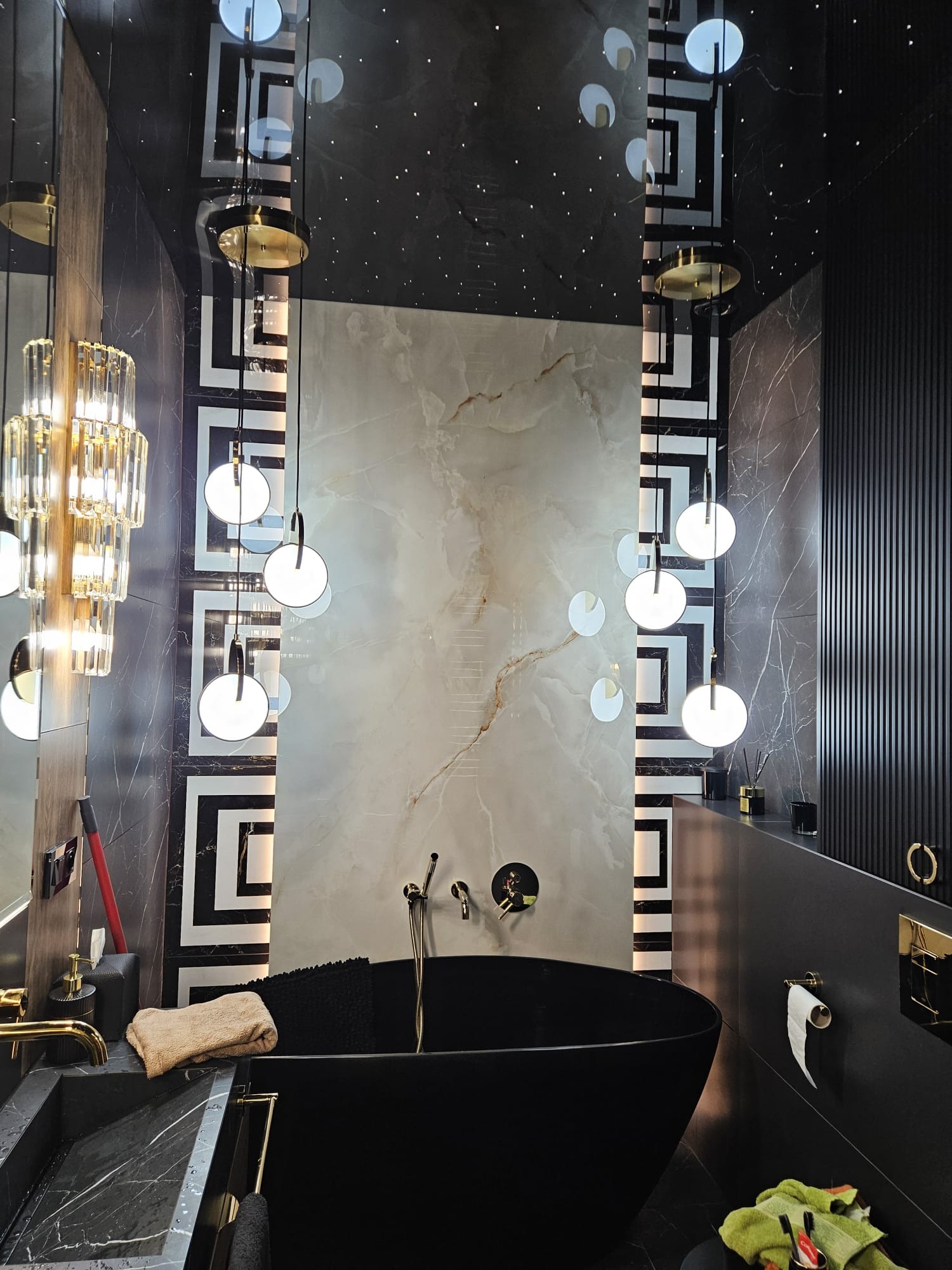 Luksusowa łazienka w ciemnej tonacji z wolnostojącą wanną, marmurowymi płytkami i dekoracyjnym oświetleniem sufitowym imitującym gwiazdy. Geometryczne wzory na ścianach.