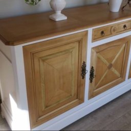 Mariusz isiu - Drewniany kredens w stylu rustykalnym z jasnym blatem i białymi bokami, zdobiony geometrycznymi wzorami na frontach drzwiczek i ciemnymi uchwytami.