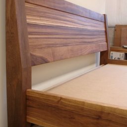 Mariusz isiu - Drewniane łóżko z wezgłowiem o wyraźnym usłojeniu, widoczne detale konstrukcyjne i naturalny odcień drewna. Minimalistyczny design, ciepłe oświetlenie.