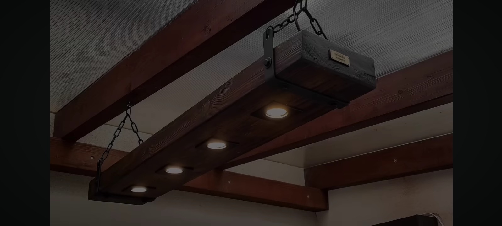 Drewniana lampa wisząca z czterema punktami świetlnymi, zawieszona na łańcuchach, w rustykalnym stylu, z widoczną strukturą drewna i metalowymi elementami.