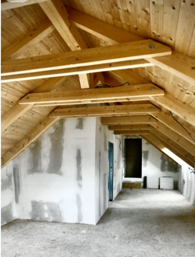 Poddasze w trakcie adaptacji: drewniana konstrukcja dachu z widocznymi belkami, oświetlenie, ściany w stanie surowym, przygotowane do dalszych prac wykończeniowych.