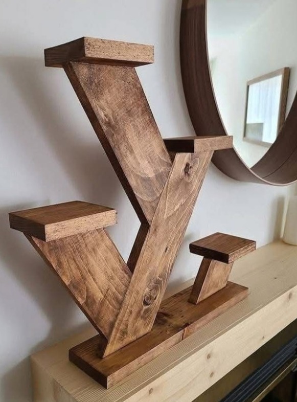 Brązowy, drewniany kwietnik o geometrycznym kształcie na tle ściany z okrągłym lustrem. Widoczne słoje drewna i detale wykonania. Dekoracja wnętrza.