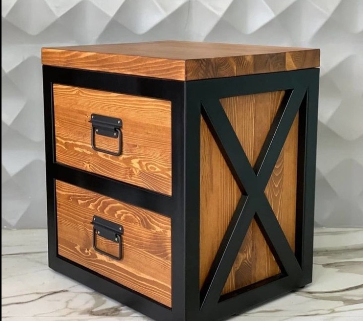 Drewniana szafka nocna z dwoma szufladami, w stylu industrialnym, z czarną metalową ramą i uchwytami. Widoczny blat z naturalnego drewna i dekoracyjne X po bokach.