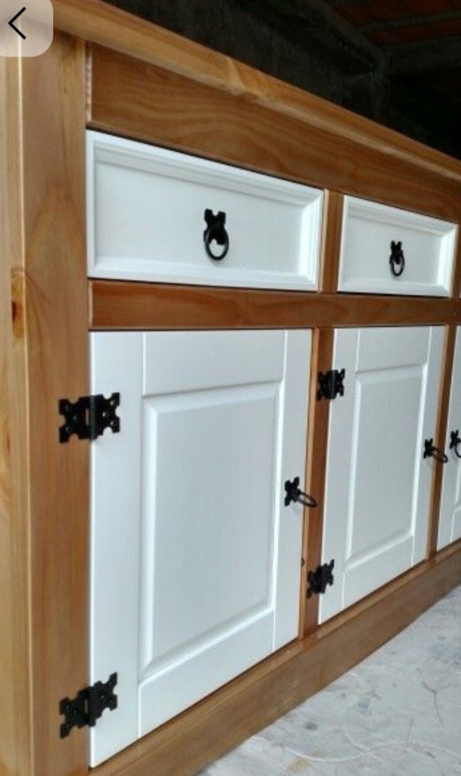 Drewniana komoda z białymi frontami i czarnymi, stylizowanymi uchwytami. Widoczne słoje drewna i detale wykończenia. Ujęcie z boku, podkreślające głębię mebla.