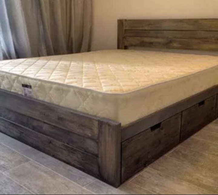 Drewniane łóżko z szufladami w stylu rustykalnym, z materacem. Widoczne szafki nocne i zasłony w tle. Ujęcie z niskiego kąta, podkreślające solidną konstrukcję.