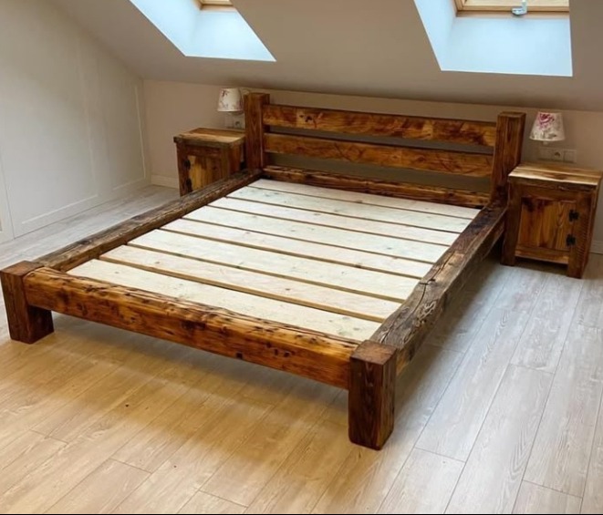 Rustykalne łóżko z drewna i szafki nocne w pokoju na poddaszu z oknami dachowymi. Widoczne słoje i naturalne niedoskonałości drewna.