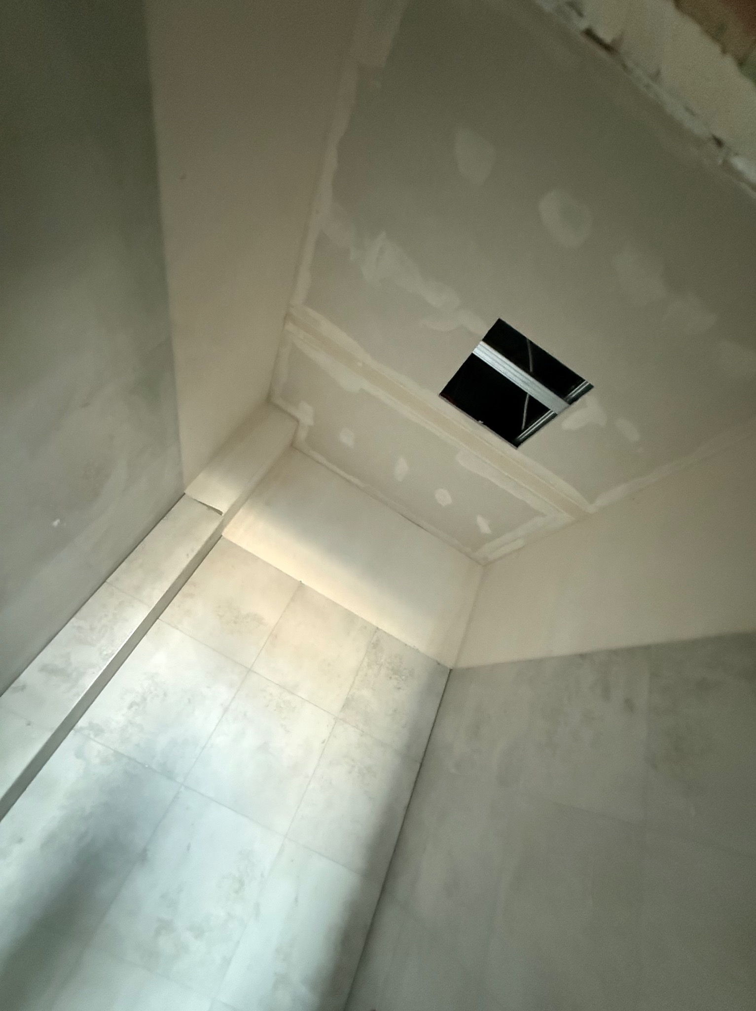 Wnętrze łazienki w trakcie remontu: widoczne płytki na ścianach i podłodze, sufit z otworem i metalową konstrukcją, ściany przygotowane do malowania.