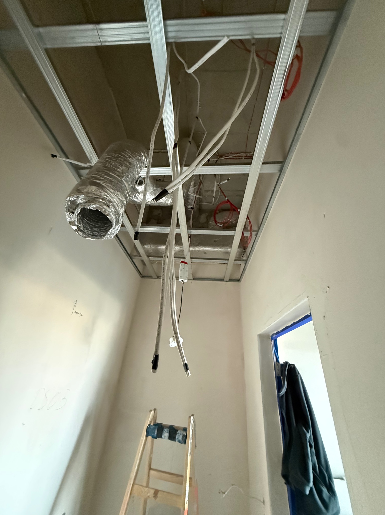 Montaż sufitu podwieszanego z widoczną instalacją wentylacyjną i elektryczną. Metalowa konstrukcja, przewody i rura wentylacyjna w surowym wnętrzu.