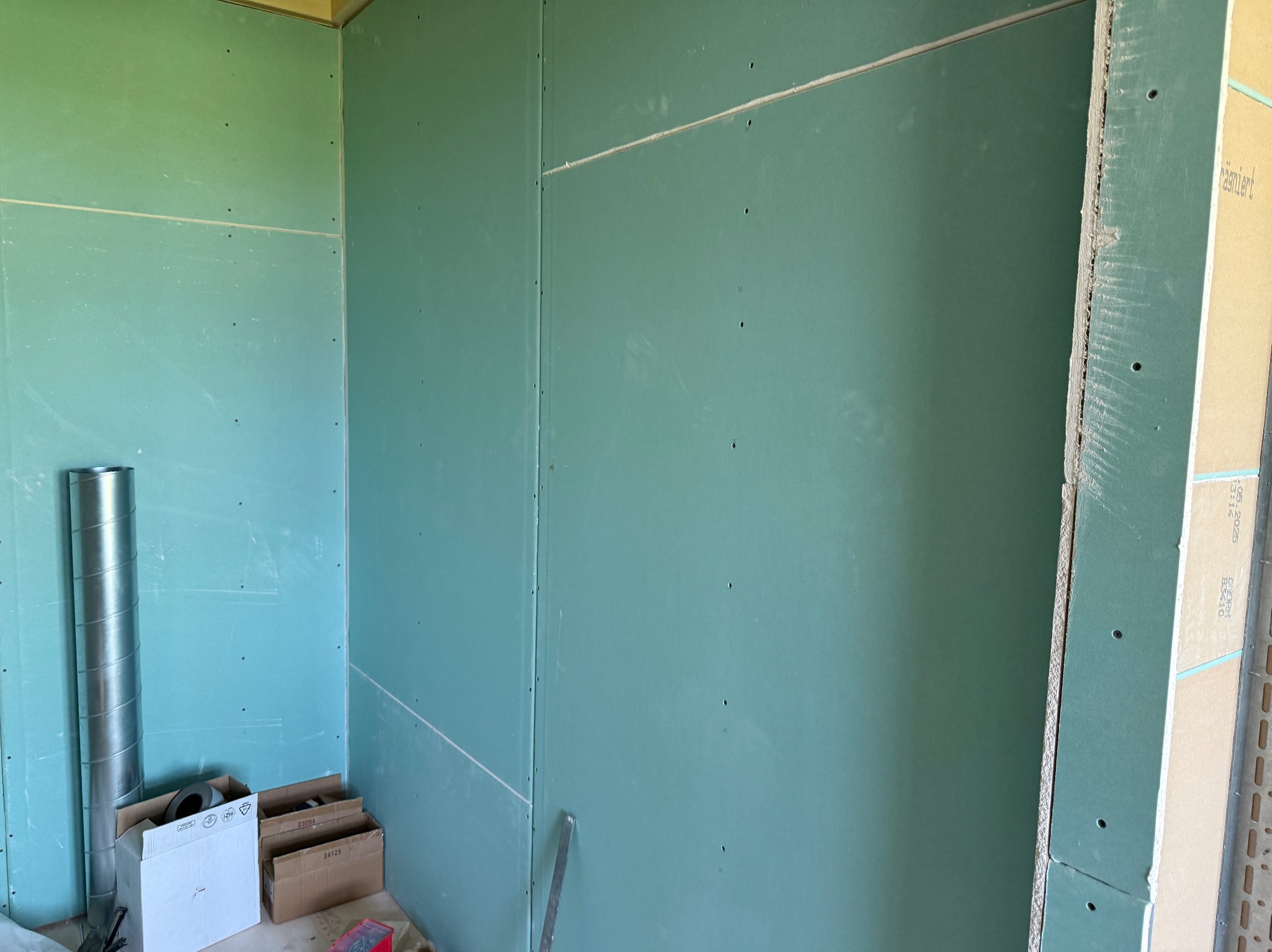 Ściana z płyt gipsowo-kartonowych w trakcie montażu w Oleśnicy. Widoczne łączenia i przygotowania do dalszych prac wykończeniowych. Elementy instalacji wentylacyjnej.