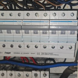 Robert Breza - Rozdzielnica elektryczna marki Hager z zainstalowanymi bezpiecznikami i przewodami. Widoczne oznaczenia i specyfikacje techniczne na urządzeniach.