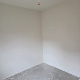 Bartosz Nowicki - Wnętrze pokoju po nałożeniu gładzi, widoczny kubeł z masą szpachlową i szpachelka. Ściany gładkie, przygotowane do malowania. Kabel zwisa z sufitu.