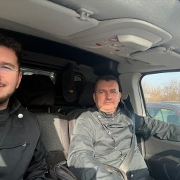 R.K.Kominiarstwo - Dwóch kominiarzy w uniformach siedzi w samochodzie, gotowych do pracy. Jeden z nich ma okulary i uśmiecha się.