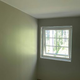 Mateusz Górski - Jasny pokój po malowaniu ścian na oliwkowy odcień, z oknem z widokiem na zieleń. Na suficie widoczny otwór na oświetlenie. Podłoga przygotowana do dalszych prac.