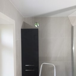 Pol-Nor Invest - Wykończona łazienka z szarymi płytkami, czarną szafką i drabiną. Widoczny fragment kabiny prysznicowej. Minimalistyczny design.